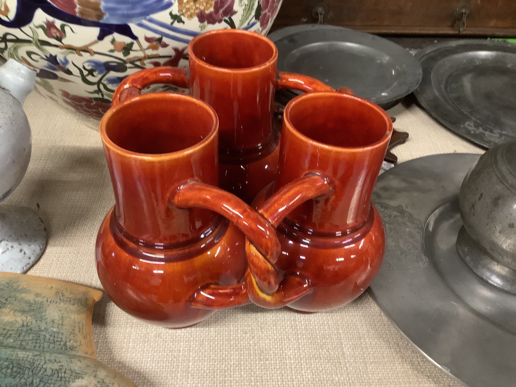 A Burmantofts Pottery three section fuddling cup with interwoven handles in dark burnt orange, stamped with marks to base, height 21cm